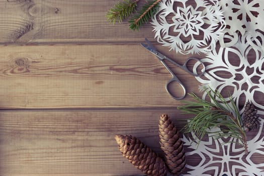 handmade paper snowflakes Christmas tree branches and fir-cones on wooden table