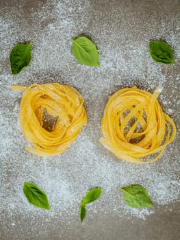 Italian food concept pasta with sweet basil with flour setup on concrete background. Homemade tagliatelle. Raw pasta on the concrete background. Food background top view .