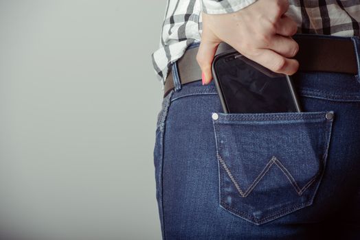 Woman takes out smartphone of her rear pocket of jeans