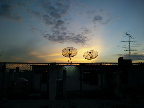 cityscape with parabolic satellite dishes at building roof and sunset background