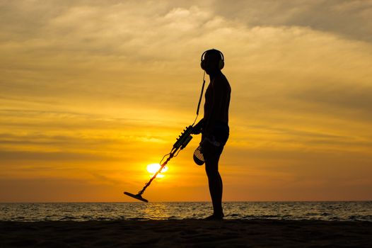a treasure hunter with Metal detector on sunset on the beach