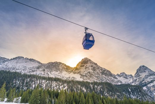 Cable car route going over the Austrian alps mountains with their fir forests, while the sun sets down behind the peaks. Image taken in Ehrwald, Austria.