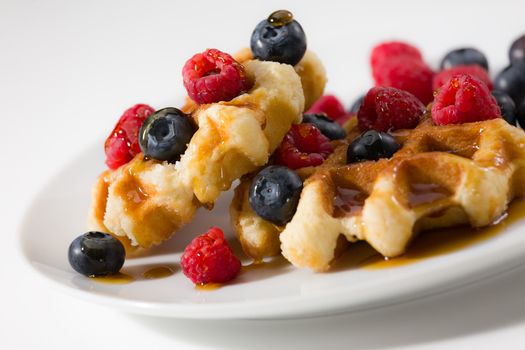 Close-up of waffles with berries and maple syrup over a white plate