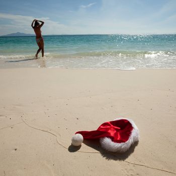 Closeup christmas hat on a white stropical sandy sea beach ans woman in bikini