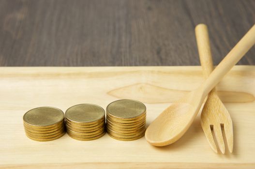 Close up step of gold coins and spoon with fork place on wooden tray with wood background.