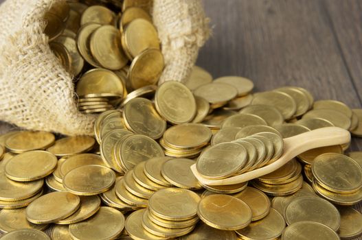 Close up gold coins in wooden spoon with brown sack of gold coins on wood background.