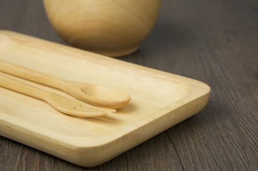 Close up wood spoon and fork place on wooden tray have blur cup as background on wood table.