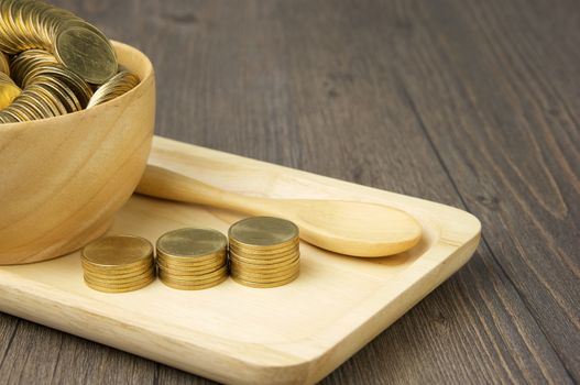 Close up step of gold coins and spoon with coins in cup place on wooden tray with wood background.