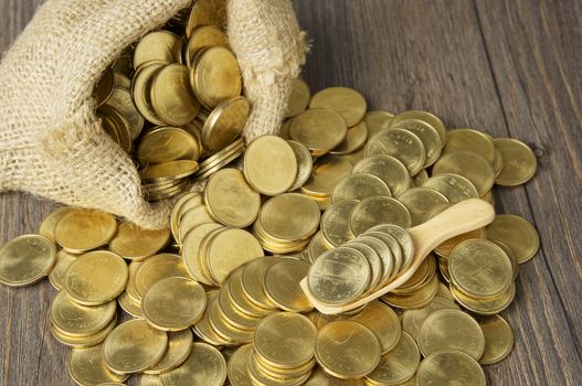 Gold coins in wood spoon with brown sack of gold coins on wooden background.