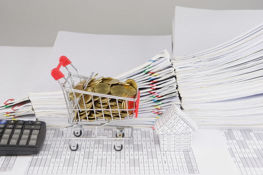 Shopping cart with gold coins and house with calculator on finance account have blur pile overload document of report and receipt with colorful paperclip as background.