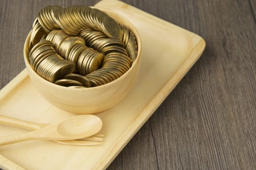 Stack of gold coins in cup place on wooden tray with spoon and fork on wood background.