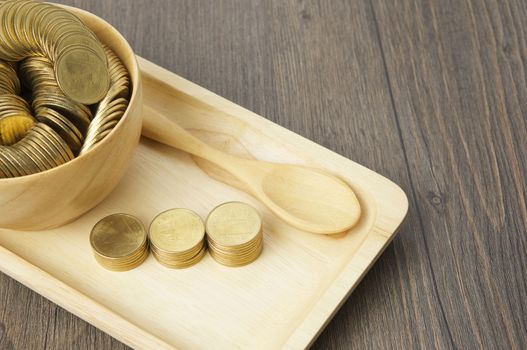 Step of gold coins and spoon with coins in cup place on wooden tray with wood background.