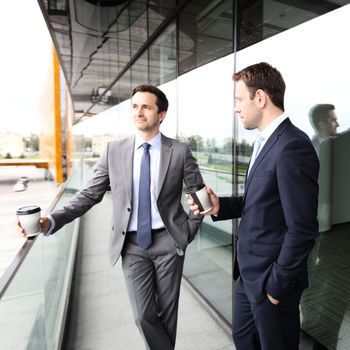 Two business people with coffee chatting on balcony of office building