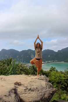 a young man standing on a rock outdoors on Phi Phi Don Island, Thailand with a bay view from above.