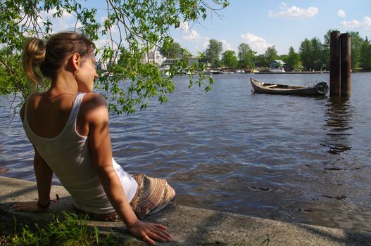 a girl sitting on pier and looking at the river. Woman relaxing by a lake.
