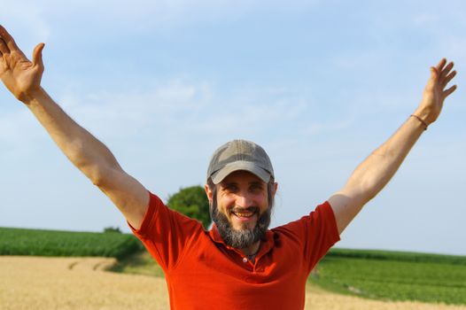 a happy bearded man raised up his hands to the sky in a golden summer corn filed, with open arms.
