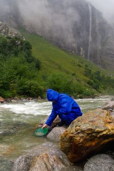 a man gold panning in a river with a sluice box during rain