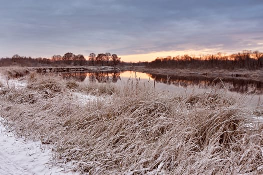 Cloudy autumn dawn. First snow in the autumn river. Belarus autumn scene