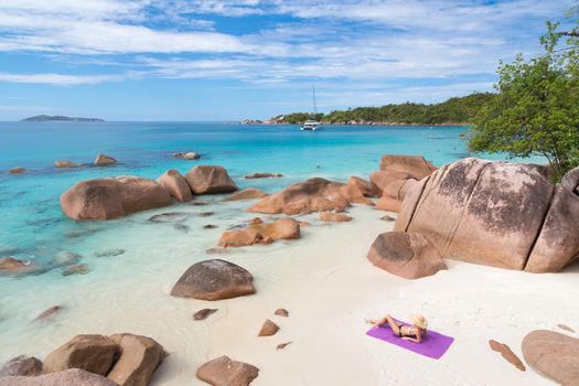 Woman wearing black bikini and beach hat, sunbathing at Anse Lazio beach on Praslin Island, Seychelles. Summer vacations on picture perfect tropical beach concept.