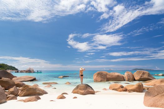 Woman wearing black bikini and beach hat, enjoying amazing view on Anse Lazio beach on Praslin Island, Seychelles. Summer vacations on picture perfect tropical beach concept.