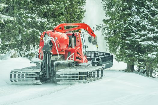 Tracked snow groomer on a snowy road, passing through the alpine forests, in the Austrian Alps, in Reutte district