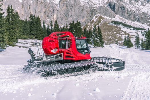 Alpine scenery with a modern tracked machine grooming snow and the rocky Austrian Alps in background