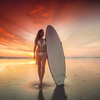 Beautiful sexy surfer girl on the beach at sunset