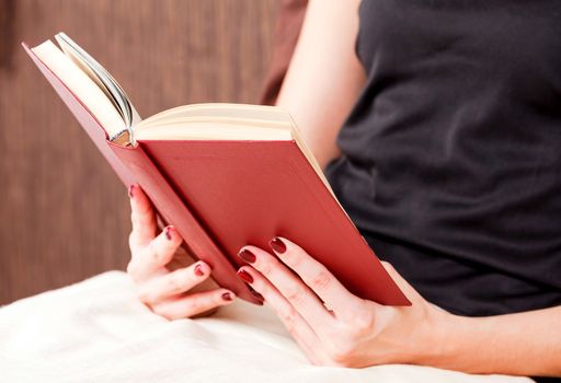 close up of young woman reading book in bed