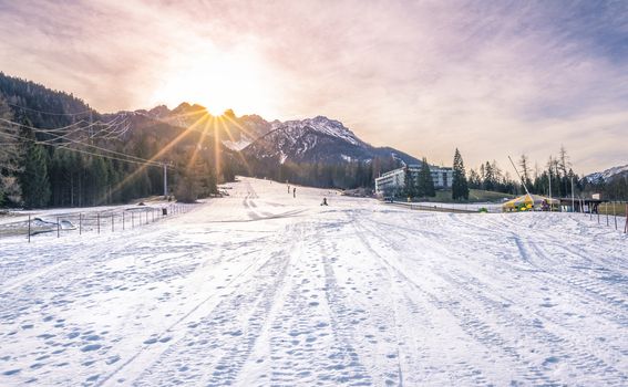 Winter landscape with a ski piste, the Austrian Alps mountains and a bright sun. Image taken in Austria.