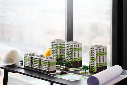 Model of apartment house, blueprint and hardhat on table in office