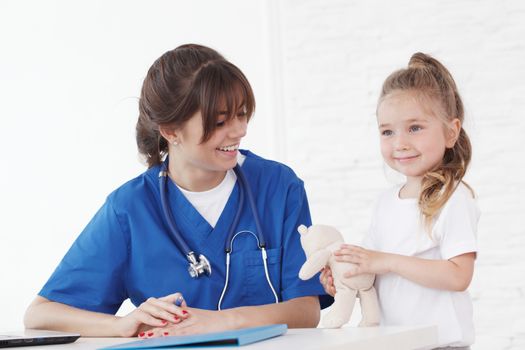 Young smiling female doctor and her little patient with teddy bear