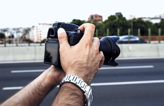 Man's hands holding photo camera near the road