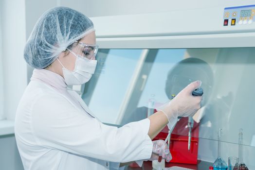 Woman scientist in a white protective clothing conducts research in a lab