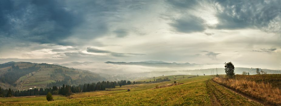 Cloudy morning in mountains. Autumn village on hillsides. Alpine scene