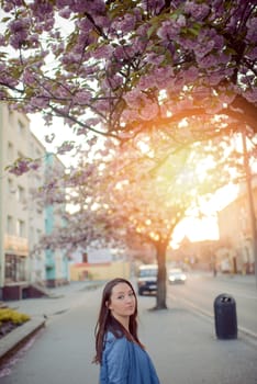 Outdoors portrait of beautiful smiling woman model in pink blossoms on spring day.