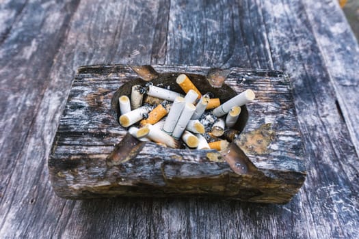 Cigarette butts with ash in ashtray on grey wooden table.