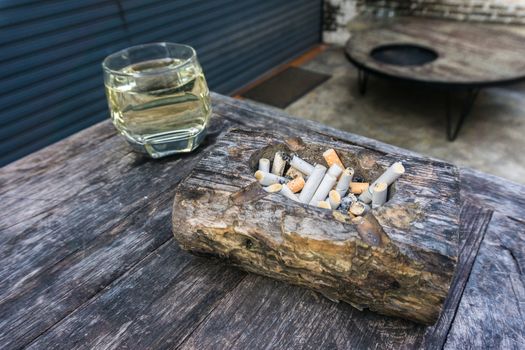 Cigarette butts with ash in ashtray on grey wooden table.