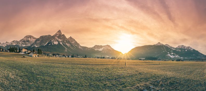 Alpine panorama with the Austrian Alps, a small village and a frosty meadow, in the colors of a winter sunset.