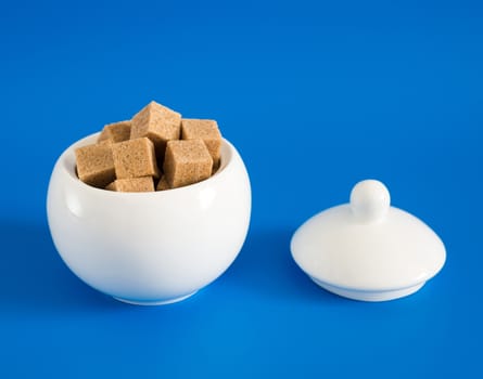 Slices of raw sugar in the sugar bowl on blue background