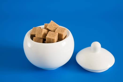 Slices of raw sugar in the sugar bowl on blue background