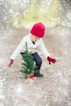 Baby Girl In Red Mittens and Cap Near Small Christmas Tree Outdoors with Snow Effect.