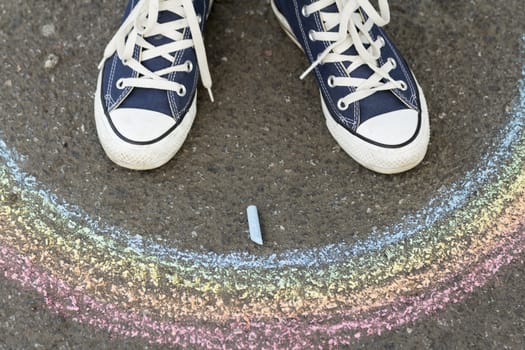 Feet in sneakers are on asphalt before drawn a rainbow