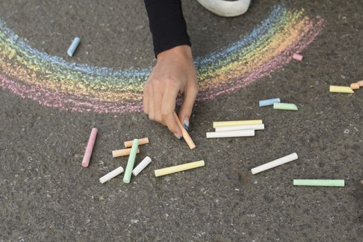 Hand draws with crayons colored Rainbow girl on the pavement