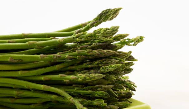 Fresh asparagus spears laid lengthwise on green plate against white background with copy space on right of horizontal photograph.  