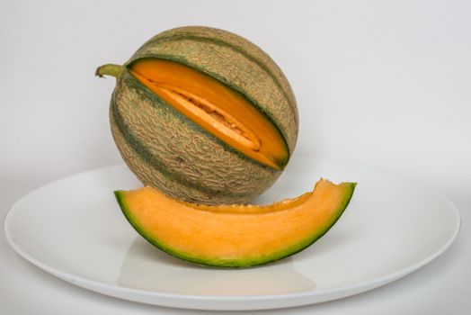 ripe melon with a slice on a plate and on white background