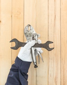 Working hand in glove holding a Spanner and Adjustable wrench with wall wood background
