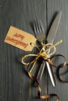 Fork and knife tied together on a wooden table background with thanksgiving tag