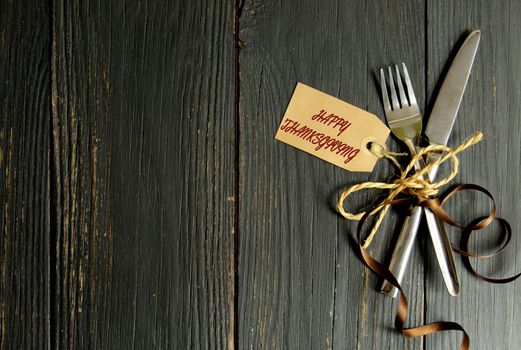 Fork and knife tied together on a wooden table background with thanksgiving tag