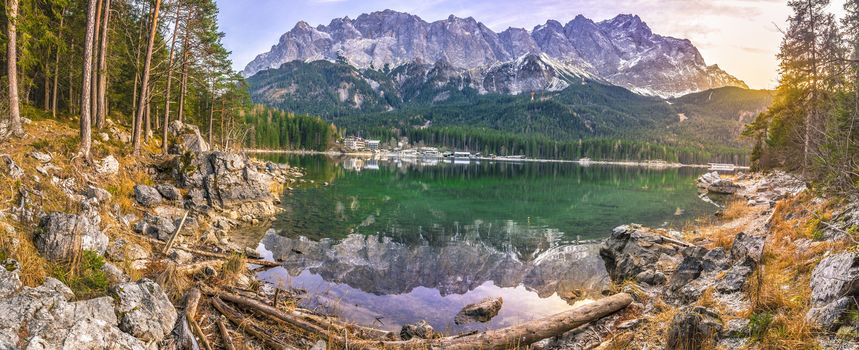 Alpine panorama with the German Alps mountains reflected in the Eibsee lake and green coniferous forest, at sunset in December.