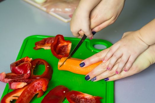 Children and mother hands cut carrot on green board